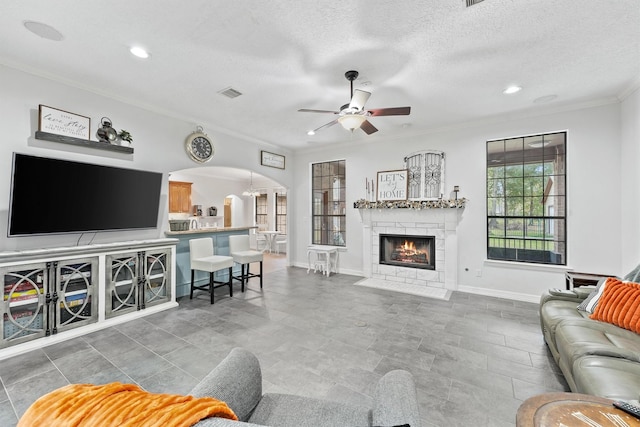 living room with a tiled fireplace, ceiling fan with notable chandelier, a textured ceiling, and ornamental molding