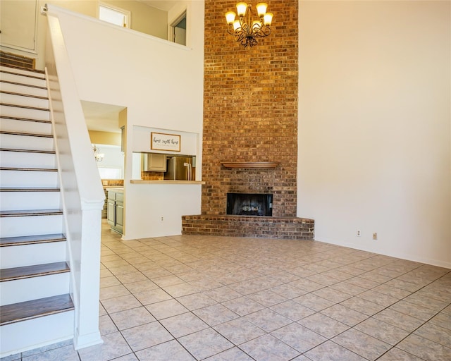 unfurnished living room featuring an inviting chandelier, a towering ceiling, light tile patterned floors, and a brick fireplace