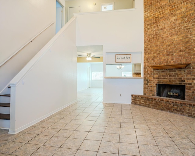 unfurnished living room featuring ceiling fan, light tile patterned flooring, a fireplace, and a high ceiling