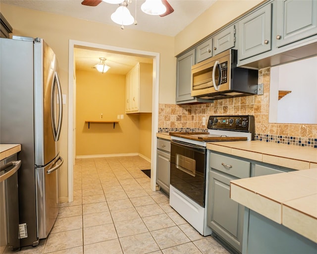 kitchen with decorative backsplash, gray cabinets, ceiling fan, light tile patterned floors, and stainless steel appliances