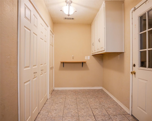 clothes washing area featuring light tile patterned flooring, cabinets, and a textured ceiling