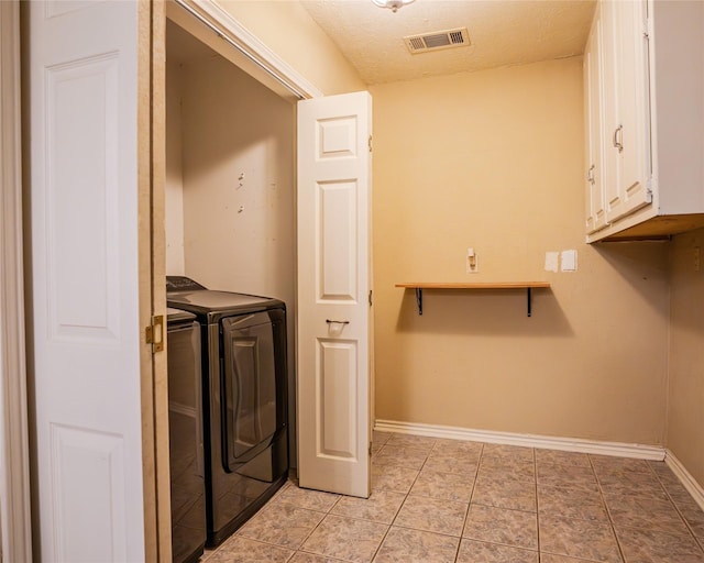 clothes washing area featuring washing machine and dryer, light tile patterned flooring, cabinets, and a textured ceiling