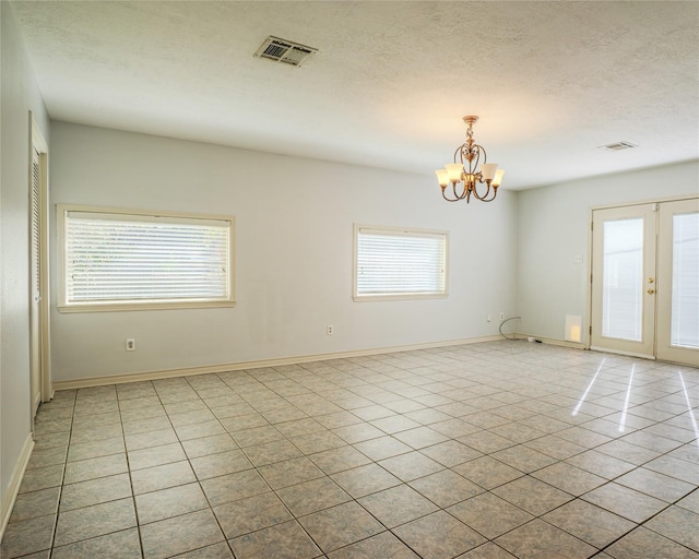 tiled empty room with a chandelier, a healthy amount of sunlight, and a textured ceiling