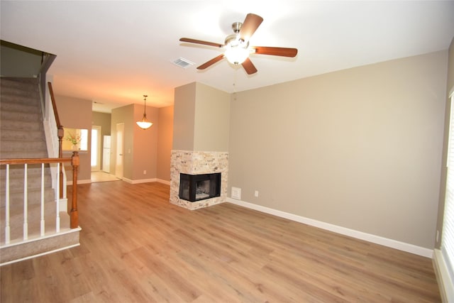 unfurnished living room with a multi sided fireplace, ceiling fan, and light wood-type flooring