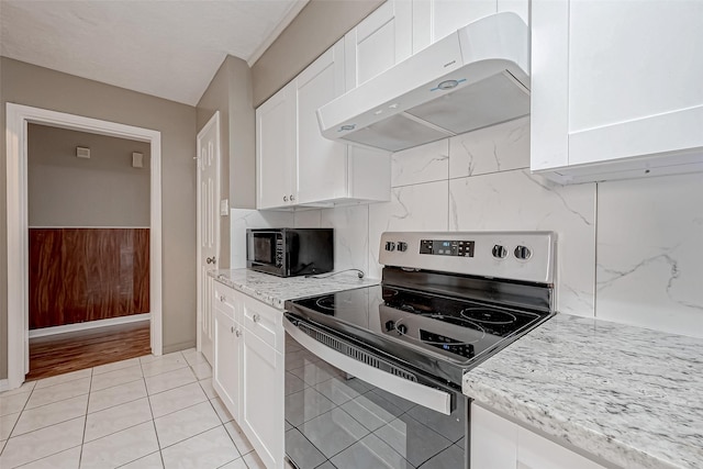 kitchen with light tile patterned floors, stainless steel range with electric stovetop, white cabinetry, light stone counters, and exhaust hood