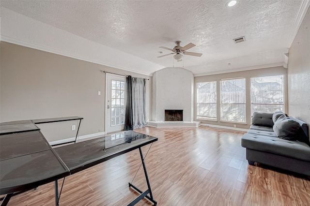 living room featuring lofted ceiling, crown molding, light hardwood / wood-style flooring, ceiling fan, and a fireplace