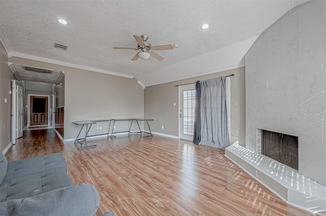 unfurnished living room featuring a tile fireplace, vaulted ceiling, light hardwood / wood-style floors, crown molding, and a textured ceiling