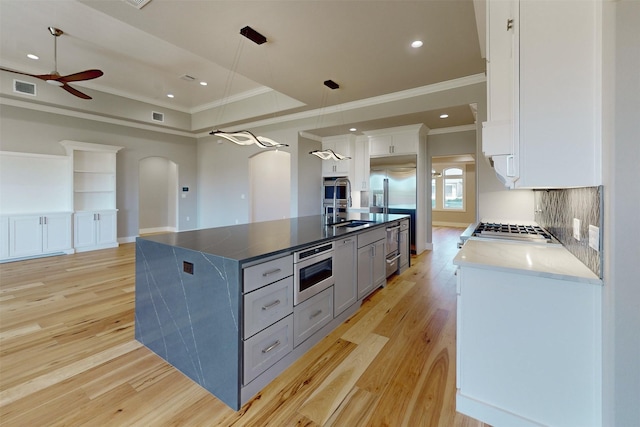 kitchen featuring light hardwood / wood-style flooring, built in appliances, decorative light fixtures, a kitchen island with sink, and white cabinets