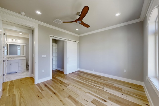 unfurnished bedroom with light hardwood / wood-style flooring, ceiling fan, a barn door, ornamental molding, and connected bathroom