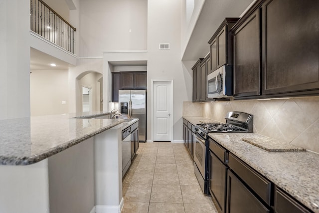 kitchen featuring decorative backsplash, light tile patterned floors, light stone countertops, appliances with stainless steel finishes, and a towering ceiling