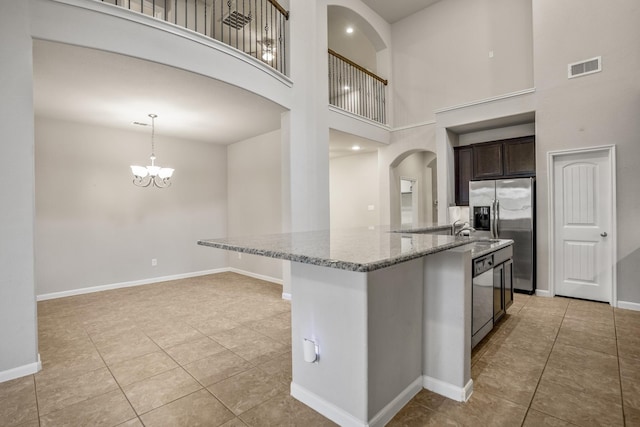 kitchen with dark brown cabinetry, hanging light fixtures, stainless steel appliances, a high ceiling, and light stone counters