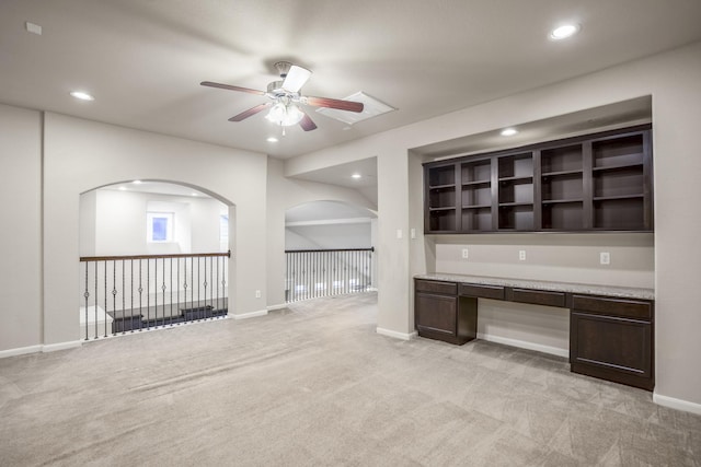 interior space with ceiling fan, light colored carpet, built in desk, and dark brown cabinetry