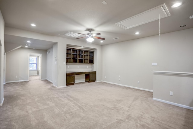 unfurnished living room featuring light carpet, built in desk, and ceiling fan