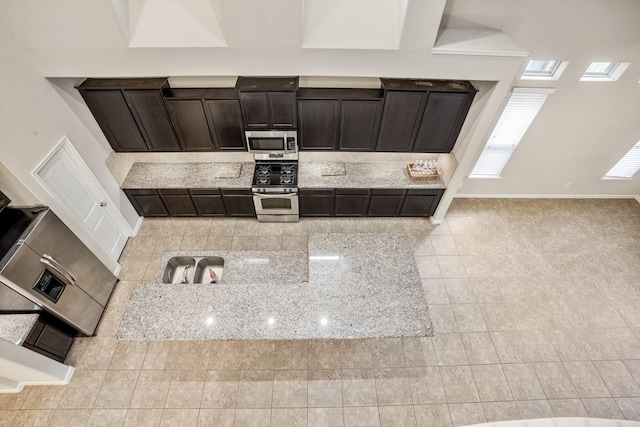 kitchen featuring light stone countertops, dark brown cabinets, light tile patterned floors, and stainless steel appliances