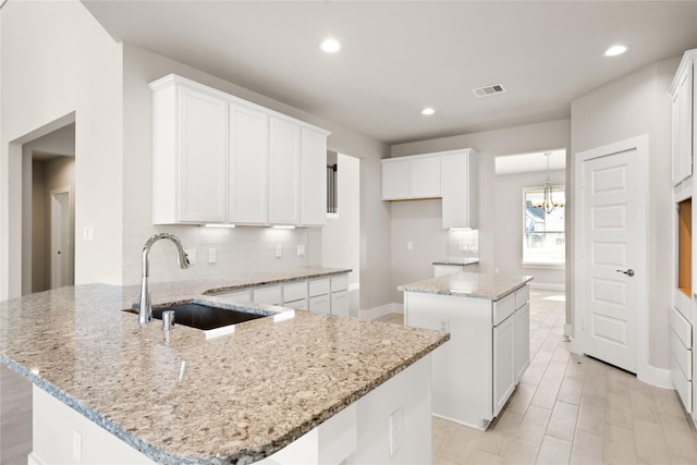 kitchen featuring white cabinets, sink, decorative backsplash, light stone countertops, and a kitchen island