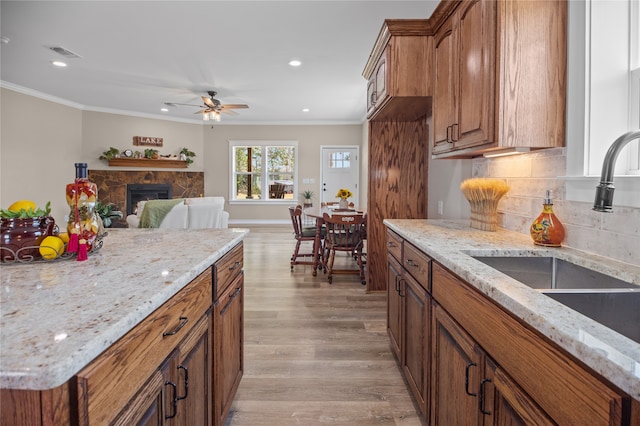 kitchen with ceiling fan, sink, light stone counters, light hardwood / wood-style flooring, and ornamental molding