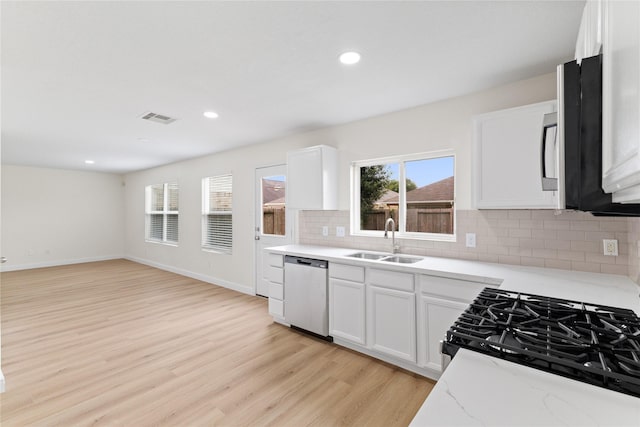 kitchen with tasteful backsplash, stainless steel dishwasher, sink, light hardwood / wood-style flooring, and white cabinets