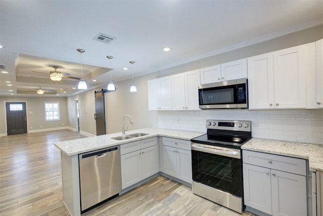 kitchen with white cabinetry, sink, a barn door, kitchen peninsula, and appliances with stainless steel finishes