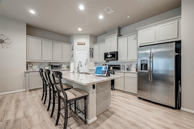 kitchen featuring a kitchen island with sink, light stone counters, light wood-type flooring, and appliances with stainless steel finishes