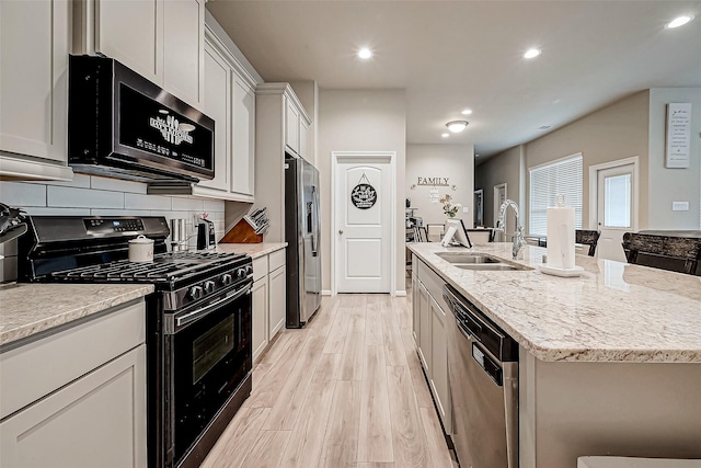 kitchen with appliances with stainless steel finishes, sink, light hardwood / wood-style flooring, white cabinetry, and an island with sink