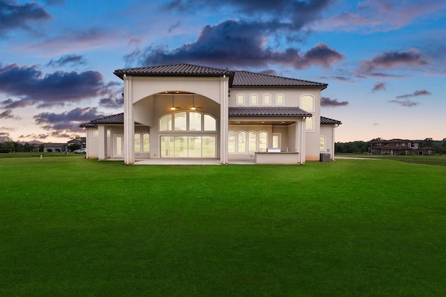 back house at dusk with ceiling fan, a yard, and a patio