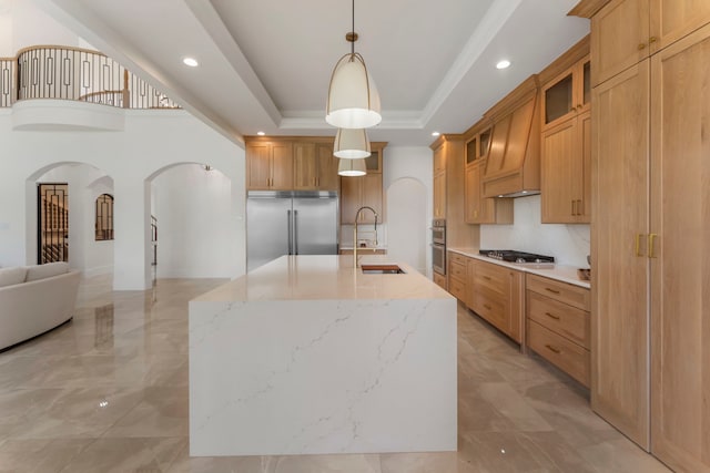 kitchen featuring pendant lighting, appliances with stainless steel finishes, sink, a raised ceiling, and a kitchen island with sink