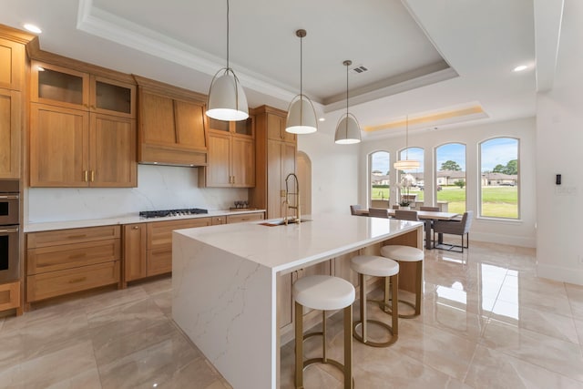 kitchen featuring a center island with sink, stainless steel appliances, a raised ceiling, and sink