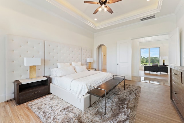 bedroom featuring ceiling fan, crown molding, light hardwood / wood-style floors, and a tray ceiling