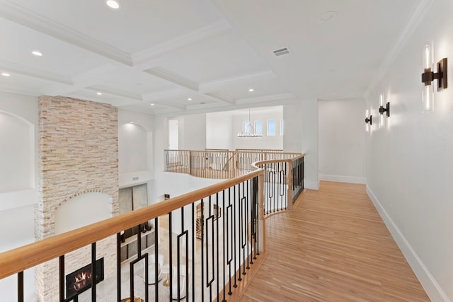 hall with coffered ceiling, a notable chandelier, light wood-type flooring, ornamental molding, and beam ceiling