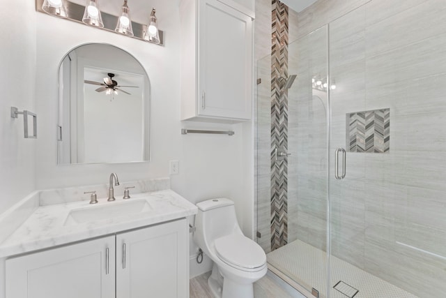 bathroom with toilet, ceiling fan, a shower with shower door, and vanity