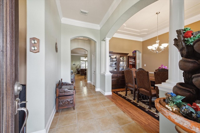 entryway featuring ornate columns, crown molding, light wood-type flooring, and an inviting chandelier