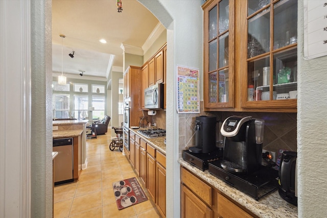 kitchen with crown molding, light stone countertops, light tile patterned floors, decorative light fixtures, and stainless steel appliances