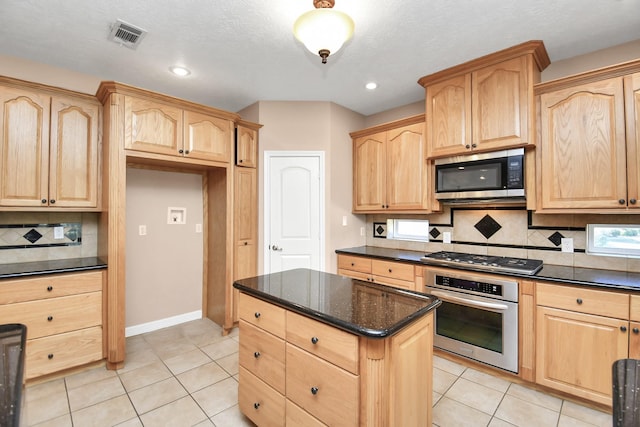 kitchen with backsplash, light tile patterned floors, dark stone counters, and appliances with stainless steel finishes