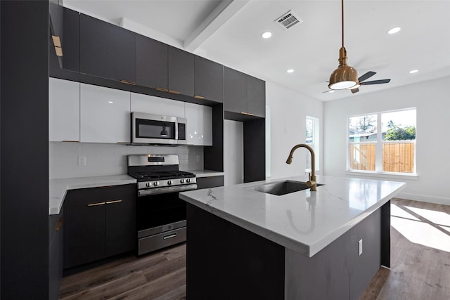 kitchen with appliances with stainless steel finishes, dark hardwood / wood-style flooring, sink, hanging light fixtures, and an island with sink