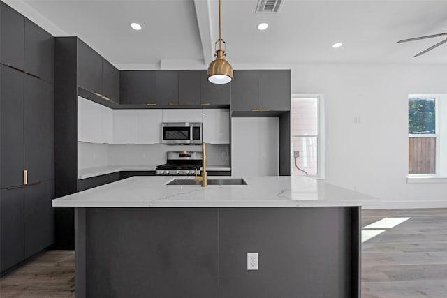 kitchen with decorative light fixtures, light hardwood / wood-style floors, stainless steel appliances, and an island with sink