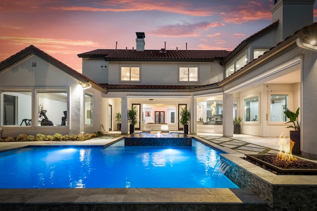 pool at dusk with pool water feature, a hot tub, a fire pit, and a patio