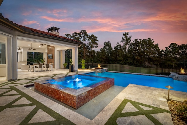 pool at dusk with an in ground hot tub, pool water feature, and a patio