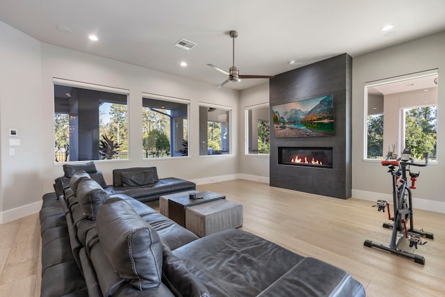 living room with a large fireplace, light hardwood / wood-style floors, plenty of natural light, and ceiling fan