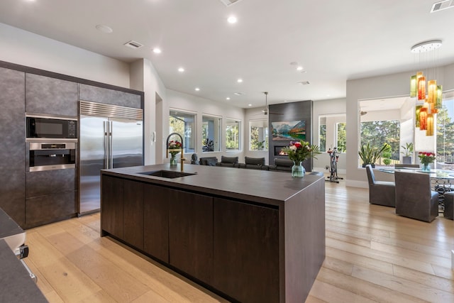 kitchen with built in appliances, light hardwood / wood-style flooring, and a kitchen island with sink