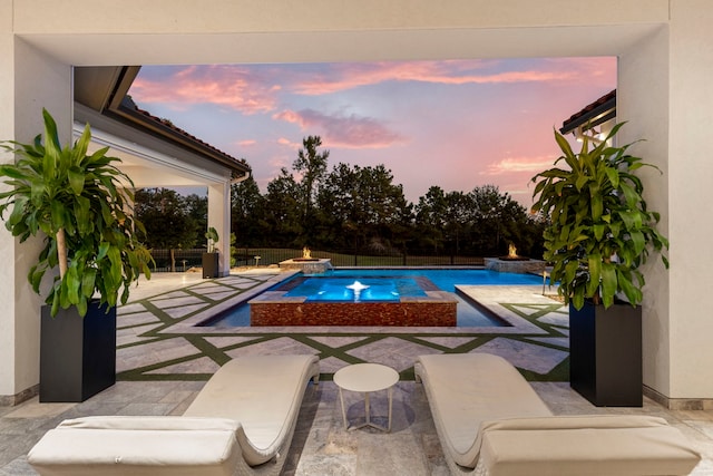 pool at dusk with a patio area, an in ground hot tub, and pool water feature