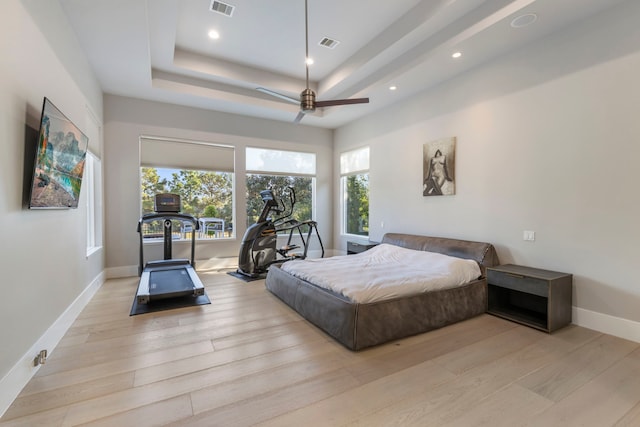 bedroom featuring a raised ceiling, ceiling fan, and light wood-type flooring