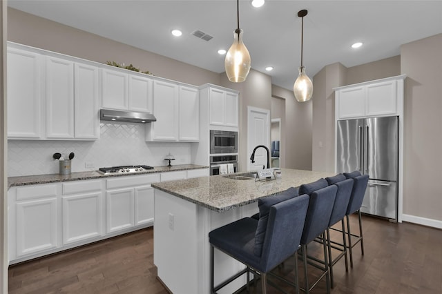 kitchen with white cabinetry, sink, stainless steel appliances, decorative light fixtures, and a center island with sink