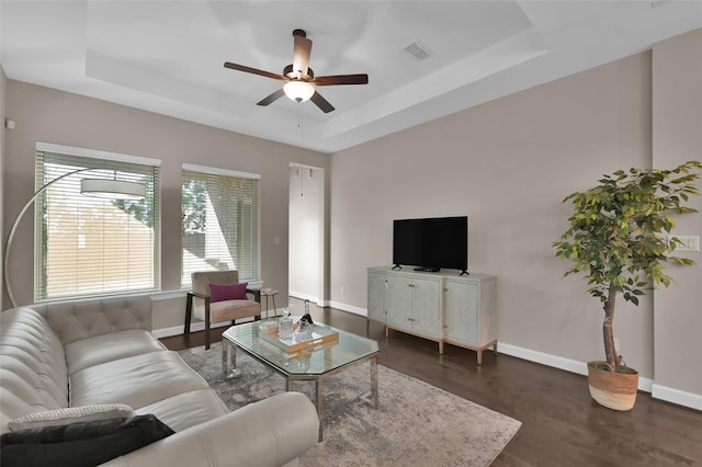 living room featuring a raised ceiling, ceiling fan, and dark hardwood / wood-style flooring