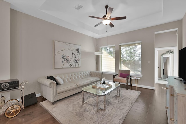 living room featuring a tray ceiling, ceiling fan, and dark wood-type flooring