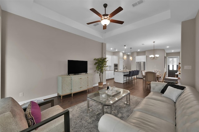 living room featuring sink, dark hardwood / wood-style floors, a raised ceiling, and ceiling fan with notable chandelier