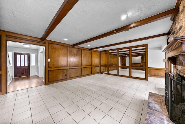 unfurnished living room with beamed ceiling, light tile patterned flooring, a textured ceiling, and a brick fireplace