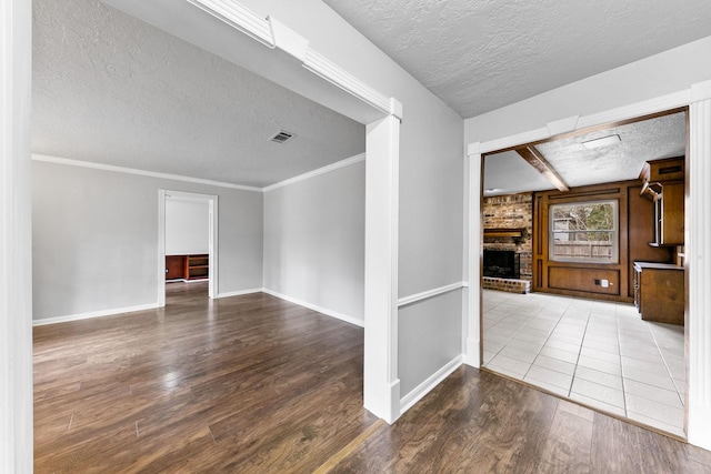 spare room featuring hardwood / wood-style floors, crown molding, a fireplace, a textured ceiling, and beamed ceiling