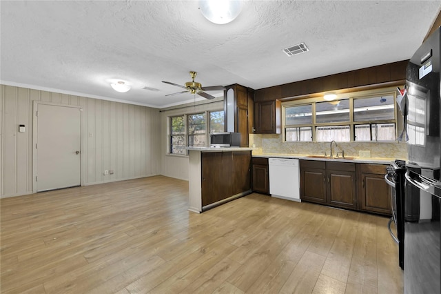 kitchen with ceiling fan, dishwasher, sink, light hardwood / wood-style floors, and wooden walls