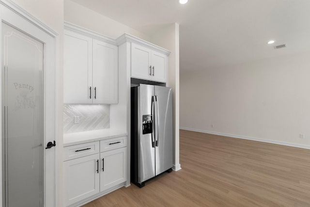 kitchen featuring white cabinets, light hardwood / wood-style floors, stainless steel fridge with ice dispenser, and tasteful backsplash