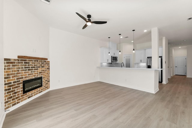 unfurnished living room with a fireplace, light hardwood / wood-style flooring, ceiling fan, and sink